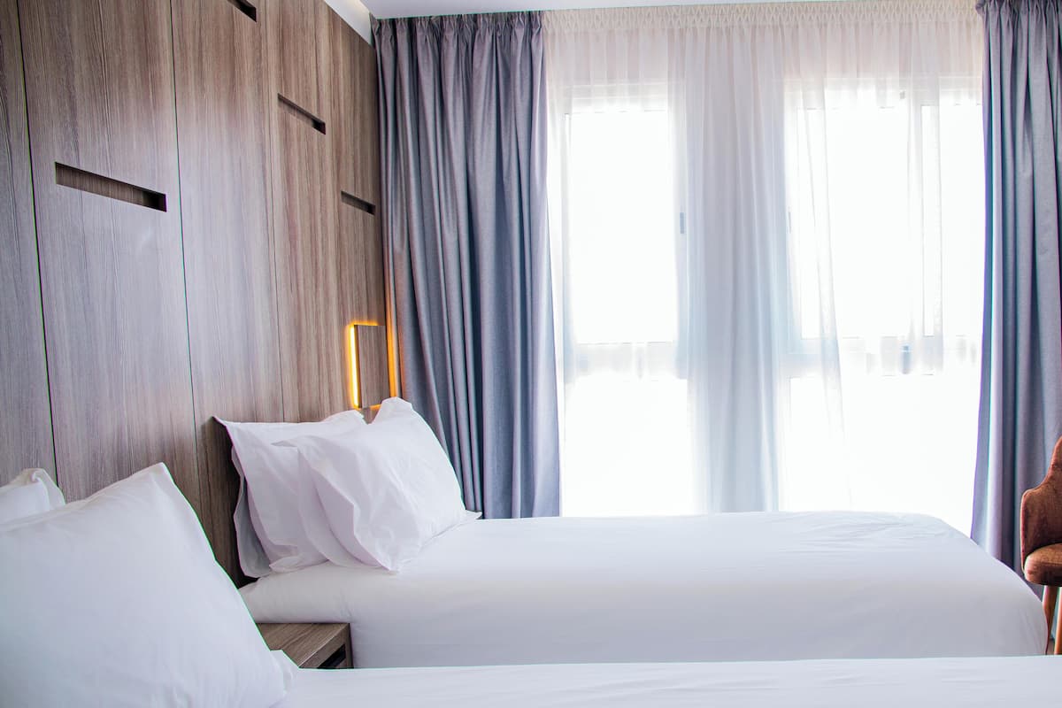 Ein Hotelzimmer mit zwei Betten, einem hölzernen Kopfteil, einem Nachttisch und einem Fenster mit Vorhängen.