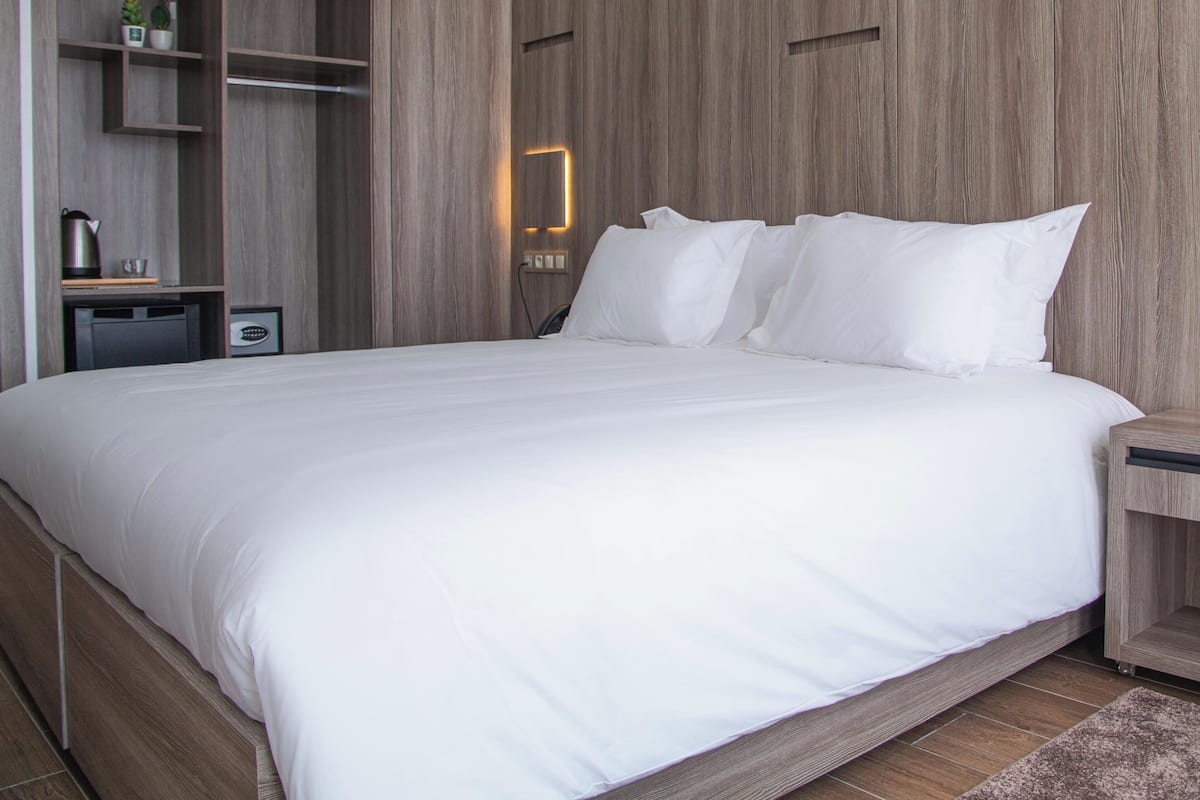 Ein modernes Hotelzimmer mit einem großen Bett, Holzwandverkleidung, integrierten Regalen und einem Nachttisch.