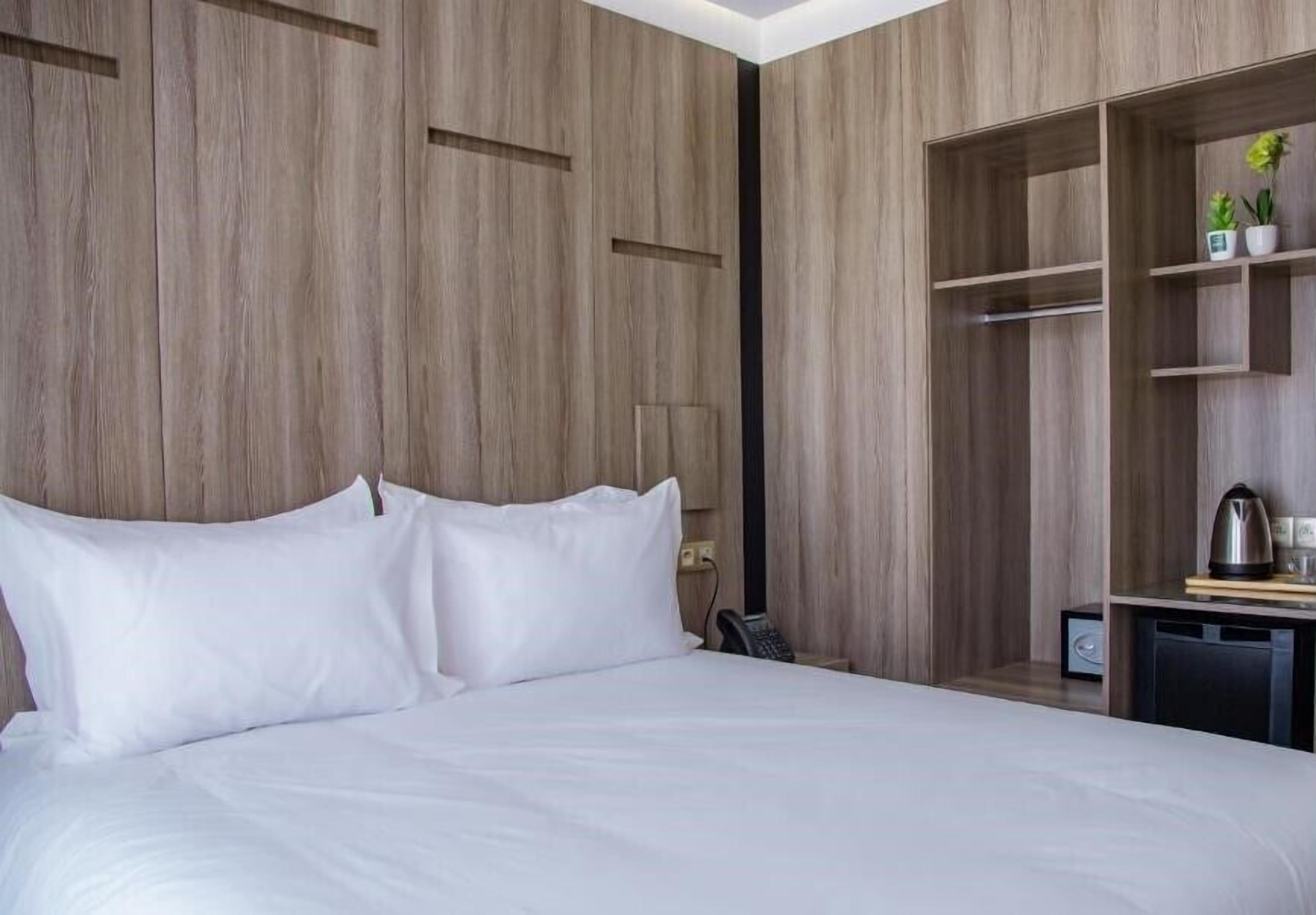 Habitación de hotel con una cama grande, paneles de madera, un escritorio con teléfono y una estantería con plantas.