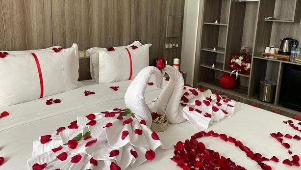 A hotel room with a wooden wall, a bed with rose petals, a swan decoration, and a minibar. - Marchica Hotel (Nador)