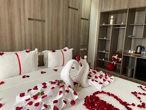 A hotel room with a wooden wall, a bed with rose petals, a swan decoration, and a minibar. - Marchica Hotel (Nador)