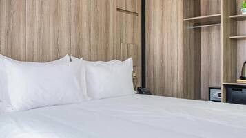 Ein Bett mit weißer Bettwäsche, ein Holzschrank und ein kleiner Schreibtisch mit Lampe.
