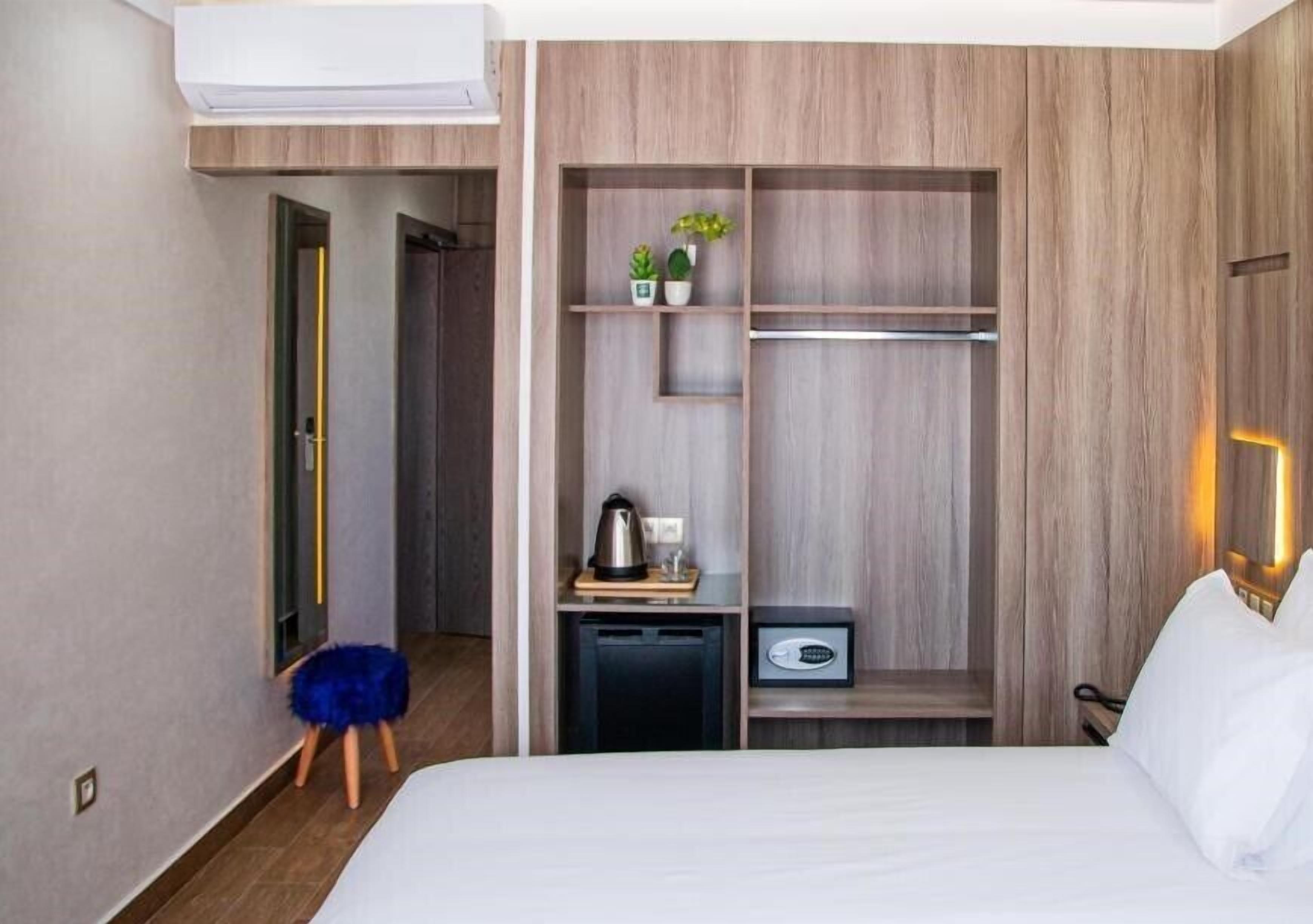 Een hotelkamer met een bed, een kledingkast, een klein tafeltje met een waterkoker en een blauwe kruk.