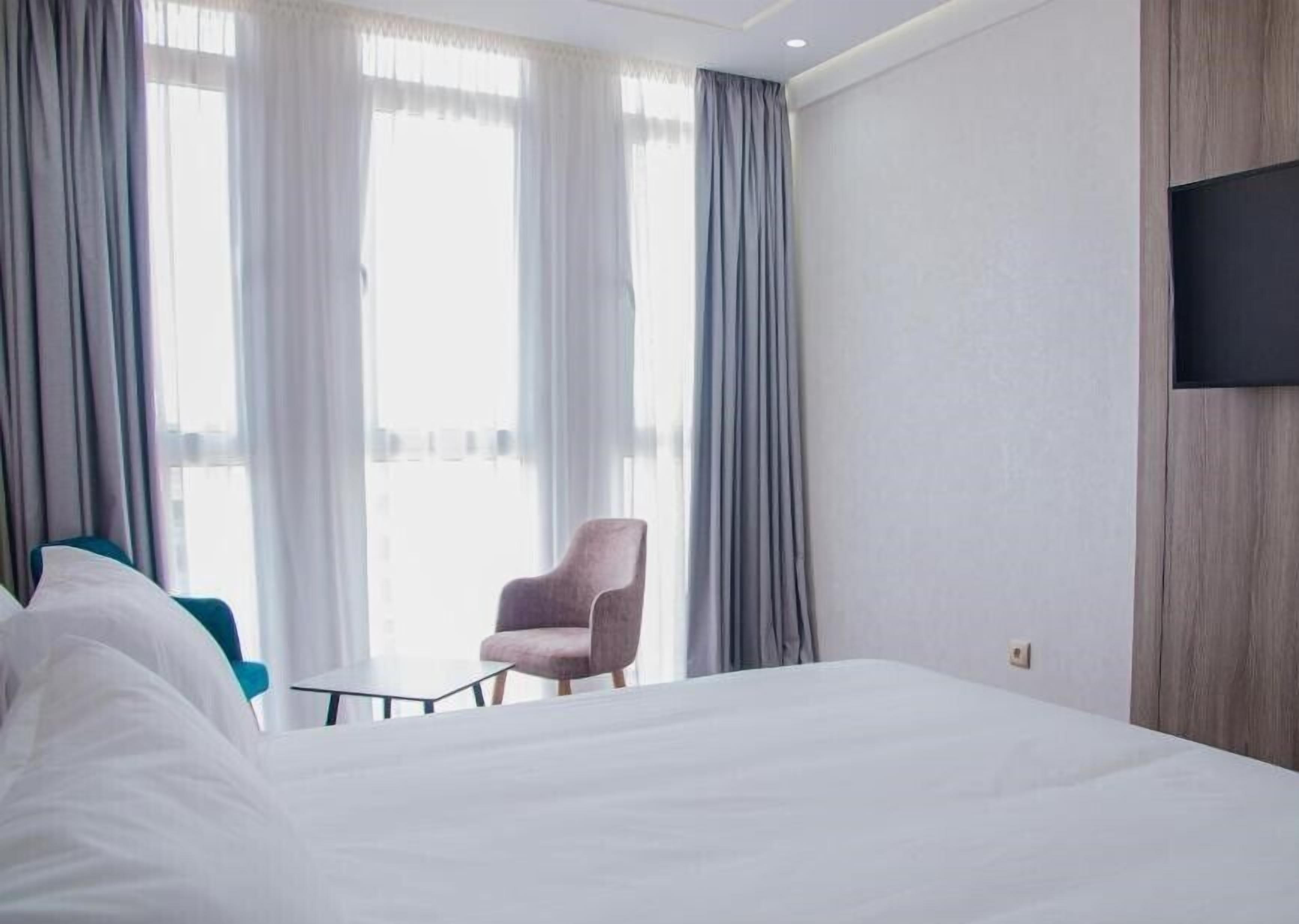 Una habitación de hotel con una cama grande, una silla, un televisor fijado a la pared y una ventana con cortinas.