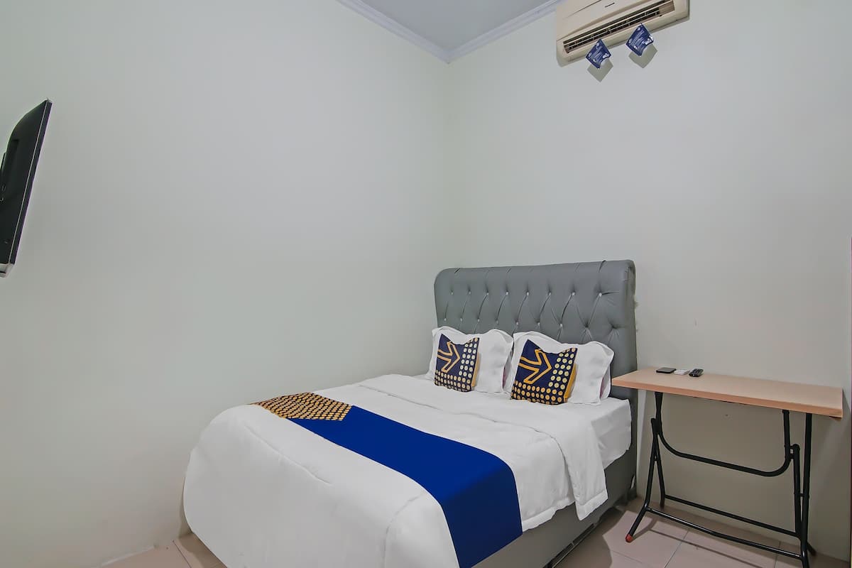 A neatly made bed with a grey headboard, white bedding, and decorative pillows. A small wooden table is positioned beside the bed.