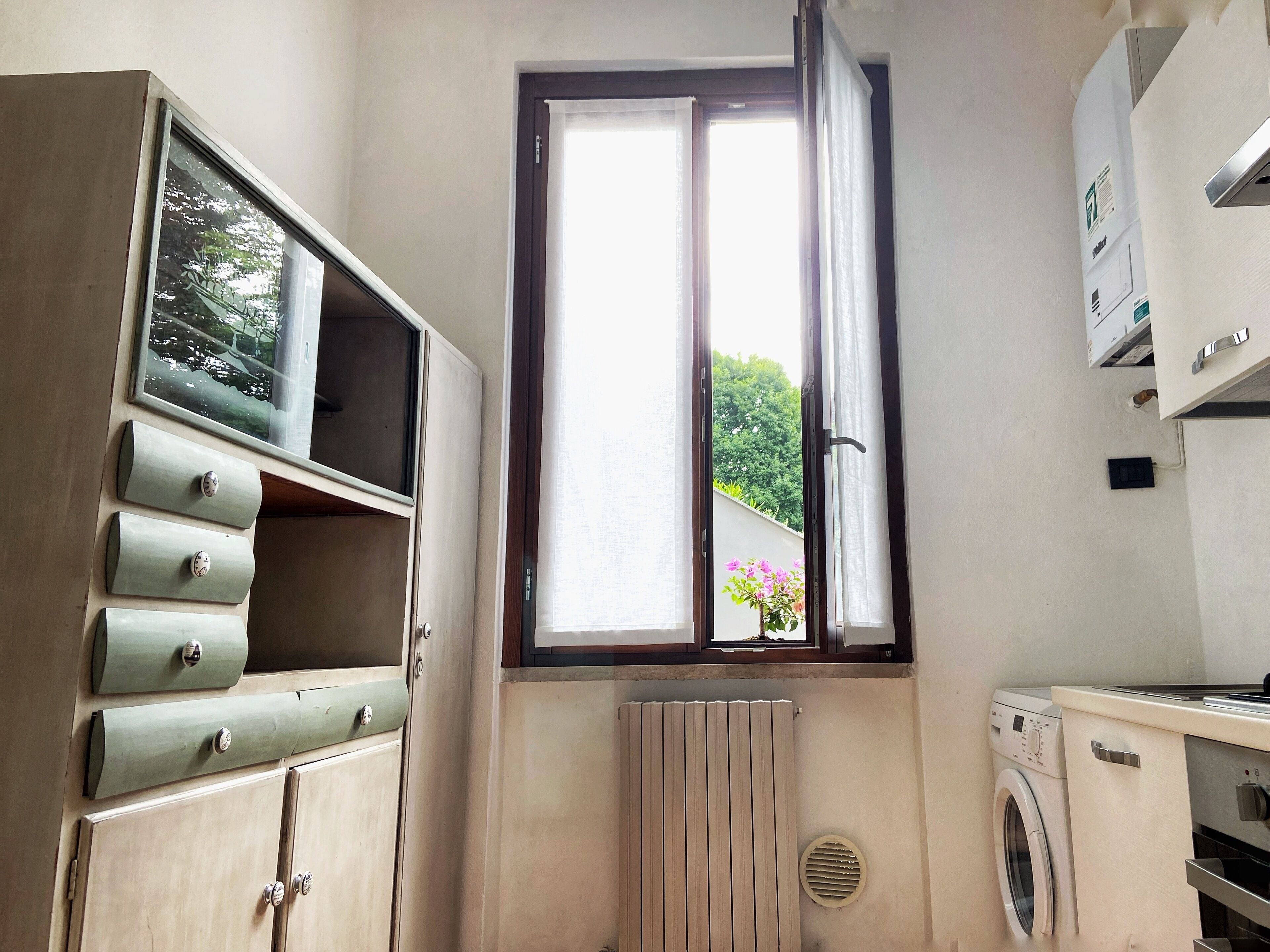 A laundry room with a window, a radiator, and a washing machine.