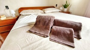 Ein ordentlich bezogenes Bett mit weißen Leinentüchern und zwei zusammengelegten braunen Handtüchern.