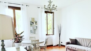 Ein Wohnzimmer mit rundem Tisch, Stühlen, einer Couch, einer Lampe, einer Pflanzvase und einem Kronleuchter.
