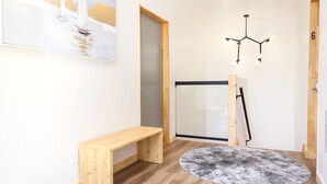 A hallway with wooden flooring, a bench, two round rugs, a painting, and a door. - Evo B&B - Adults Only, Waterfront (Northern Bruce Peninsula)