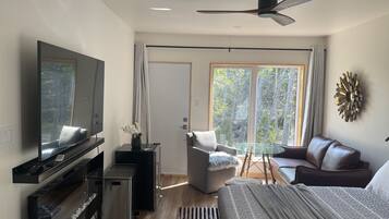 A modern bedroom with a bed, a TV, a desk, and a window with a view of trees.
