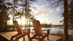 Two Adirondack chairs on a wooden deck overlooking a lake with trees and a sunset in the background. - Evo B&B - Adults Only, Waterfront (Northern Bruce Peninsula)