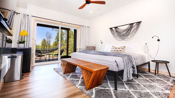 A modern bedroom with a bed, a bench, a ceiling fan, and a view of the outdoors. - Evo B&B - Adults Only, Waterfront (Northern Bruce Peninsula)