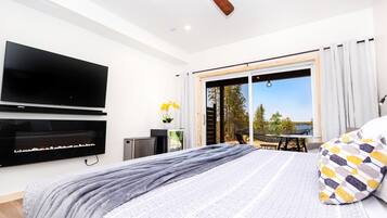 A bedroom with a bed, a flat-screen TV, a ceiling fan, a sliding glass door to a balcony, and a view of the outdoors.