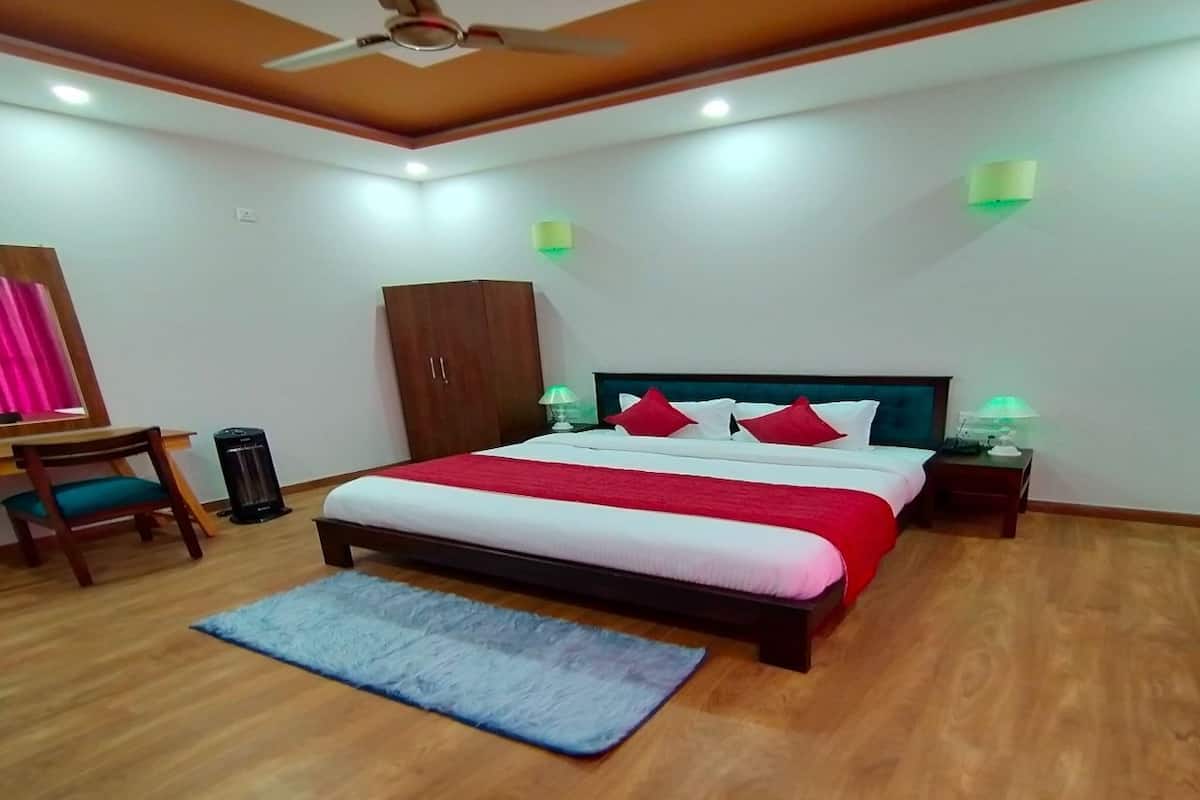 A bedroom with a bed, wooden floor, ceiling fan, bedside lamps, and a desk with a chair.