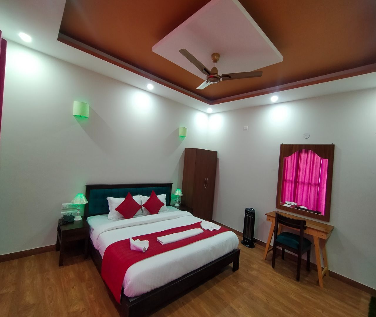 A bedroom with a bed, nightstands, a desk, a wardrobe, a ceiling fan, and a mirror.