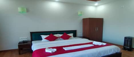 A neatly made bed with white and red bedding, a wooden headboard, and a wooden wardrobe in a room with wooden flooring and recessed ceiling lighting.