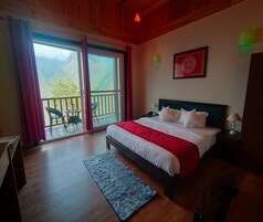 A bedroom with a large bed, a balcony with chairs, and a mountain view.