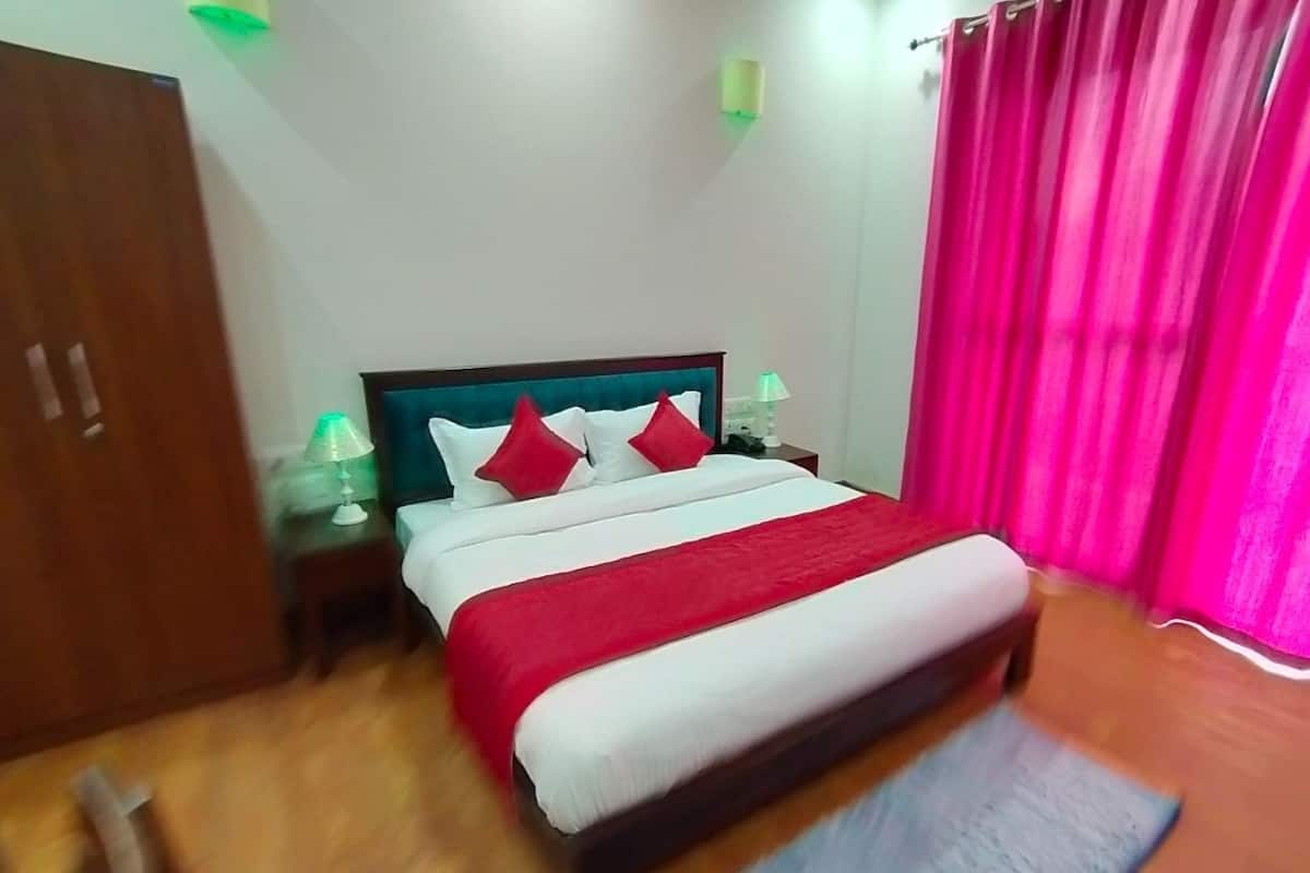 A neatly made bed with red and white bedding, a wooden floor, a nightstand with a lamp, and a wooden wardrobe.