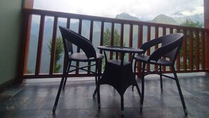 En balkon med to fletstole og et lille bord, med udsigt over et bjergrigt landskab.