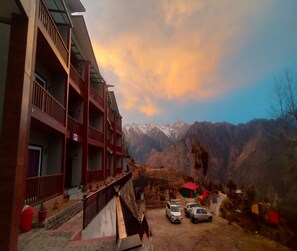 Un immeuble à plusieurs étages doté de balcons, d’un espace de stationnement et surplombant un paysage montagneux.
