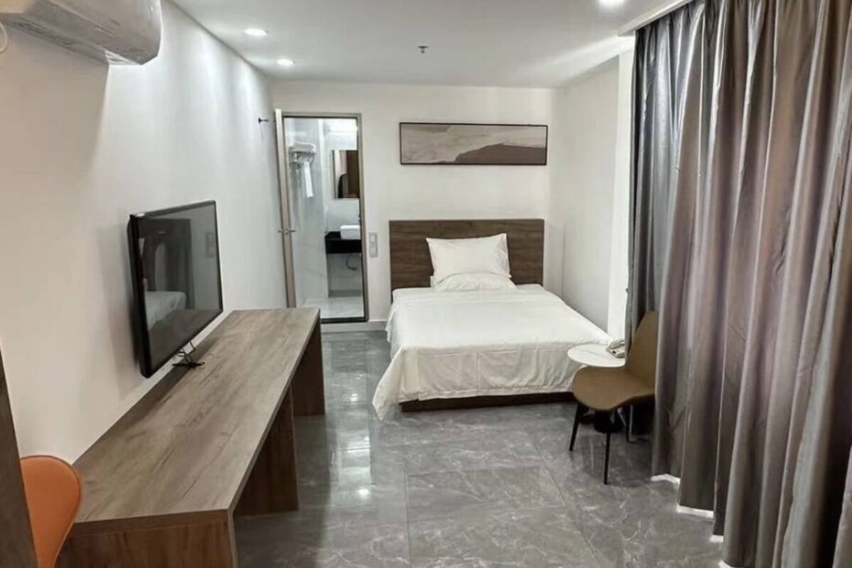 A hotel room with a bed, a desk, a chair, a television, and a bathroom visible through an open door.