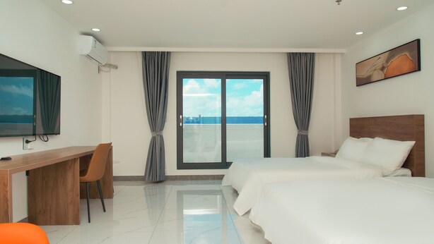 Habitación de hotel con cama, escritorio, silla, televisor y vista al cielo a través de la ventana.