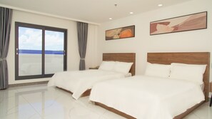 A hotel room with two beds, a large window with curtains, and artwork on the walls.