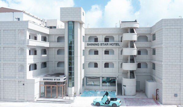 A modern hotel with a central staircase, multiple balconies, and a car parked in front.