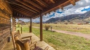Een houten hut met een overdekte veranda en uitzicht op een landelijk landschap met bergen op de achtergrond.