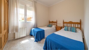 A bedroom with two beds, a wooden wardrobe, a window with curtains, and a radiator. - Mercedes: Beautiful detached house with a large garden (L'Escala)