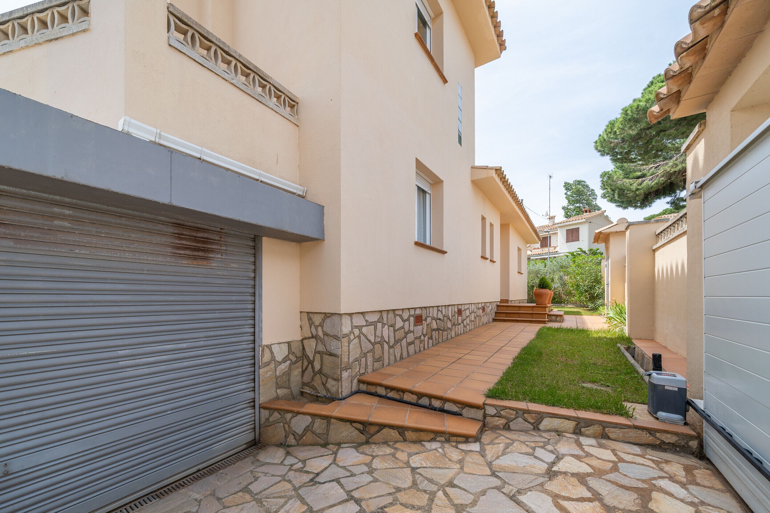 A residential building with a stone-paved courtyard, a closed garage door, and a small lawn area.