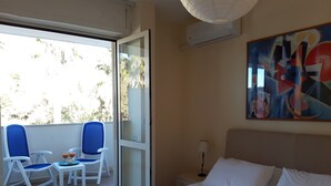 Une chambre d’hôtel avec un lit, un balcon avec des chaises, un tableau au mur et un appareil de climatisation.