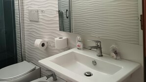 Une salle de bain avec un lavabo blanc, un bidet, des toilettes et un miroir.