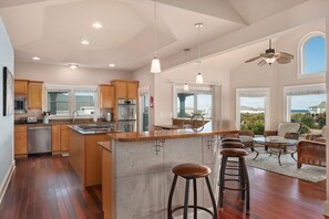 Une cuisine spacieuse avec des meubles en bois, un îlot central doté de tabourets et un coin repas avec des meubles en osier.