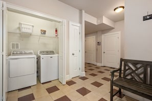 A laundry room with two washing machines, a dryer, a shelf with a basket and Tide detergent, and a bench. - Ray and TD's: Dog friendly, oceanside, pool, hot tub, theater room, elevator, EASY beach access! (Corolla)
