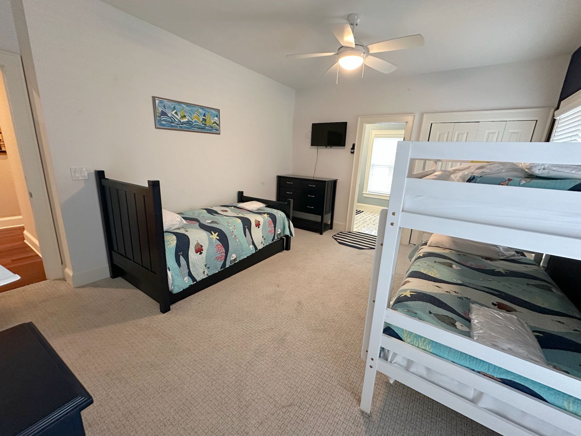 Une chambre comprenant un lit superposé, un lit simple, un bureau, une chaise, un téléviseur et un ventilateur de plafond.