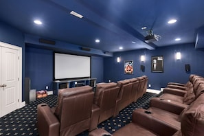 A home theater room with a large screen, reclining seats, and wall-mounted speakers. - Ray and TD's: Dog friendly, oceanside, pool, hot tub, theater room, elevator, EASY beach access! (Corolla)