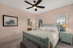 Une chambre à coucher comprenant un lit, une table de chevet, un banc, un ventilateur de plafond et un tableau encadré accroché au mur.