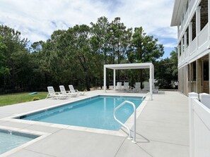 Une piscine rectangulaire avec une terrasse blanche, des chaises longues et un espace salon abrité.