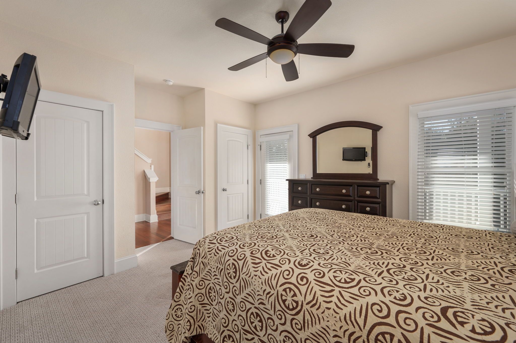 Une chambre à coucher comprenant un lit, un ventilateur de plafond, une commode et un téléviseur fixé au mur.
