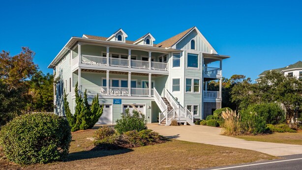 A two-story building with a balcony on the second floor, a staircase leading to the entrance, and a clear blue sky in the background.