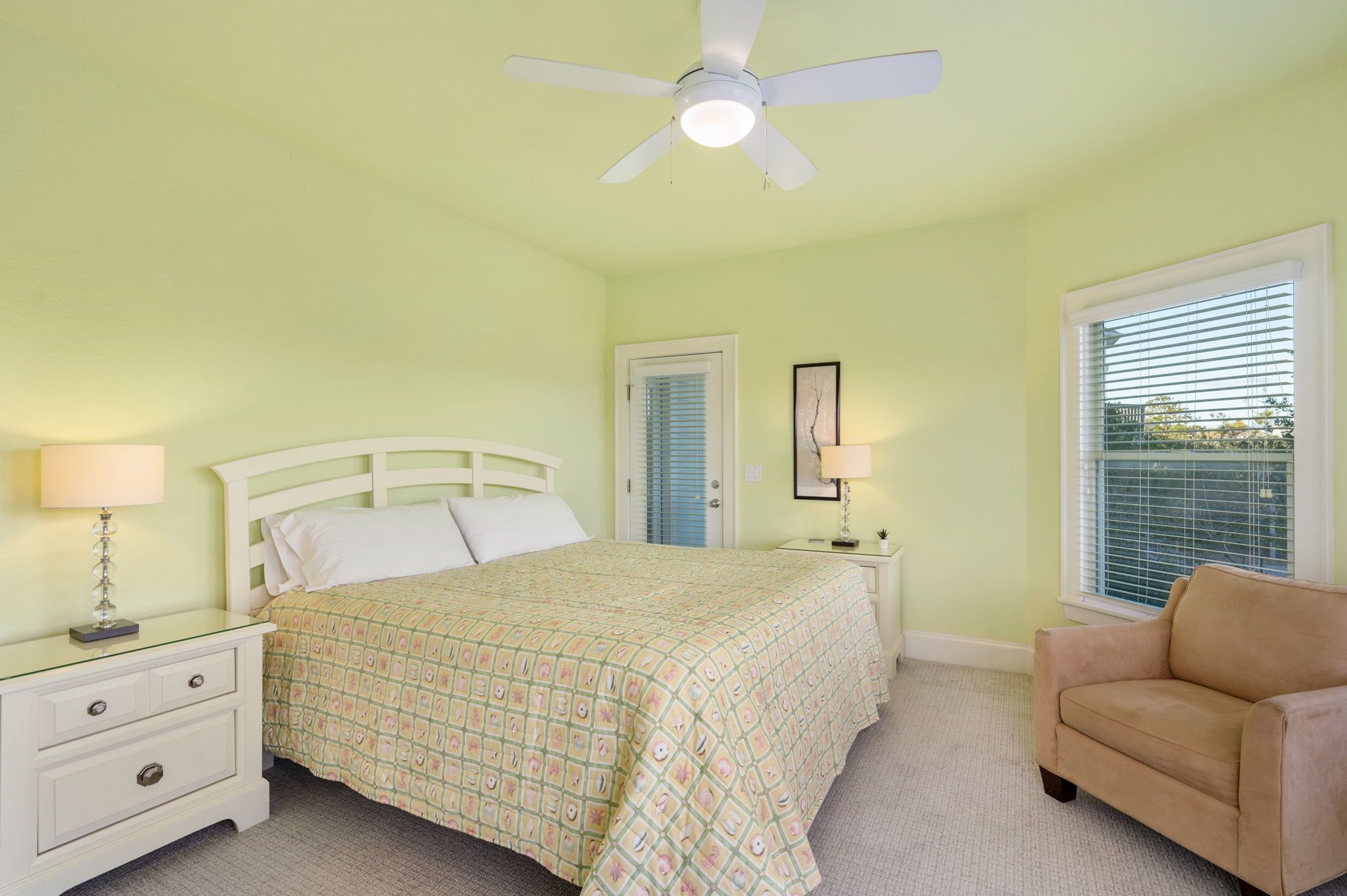 A bedroom with a bed, nightstands, a chair, a ceiling fan, and a window with blinds.