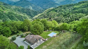 Ein Haus mit Swimmingpool, umgeben von üppiger Vegetation und Bergen im Hintergrund.