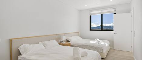 A modern bedroom with two beds, a window with a mountain view, and a wooden floor.