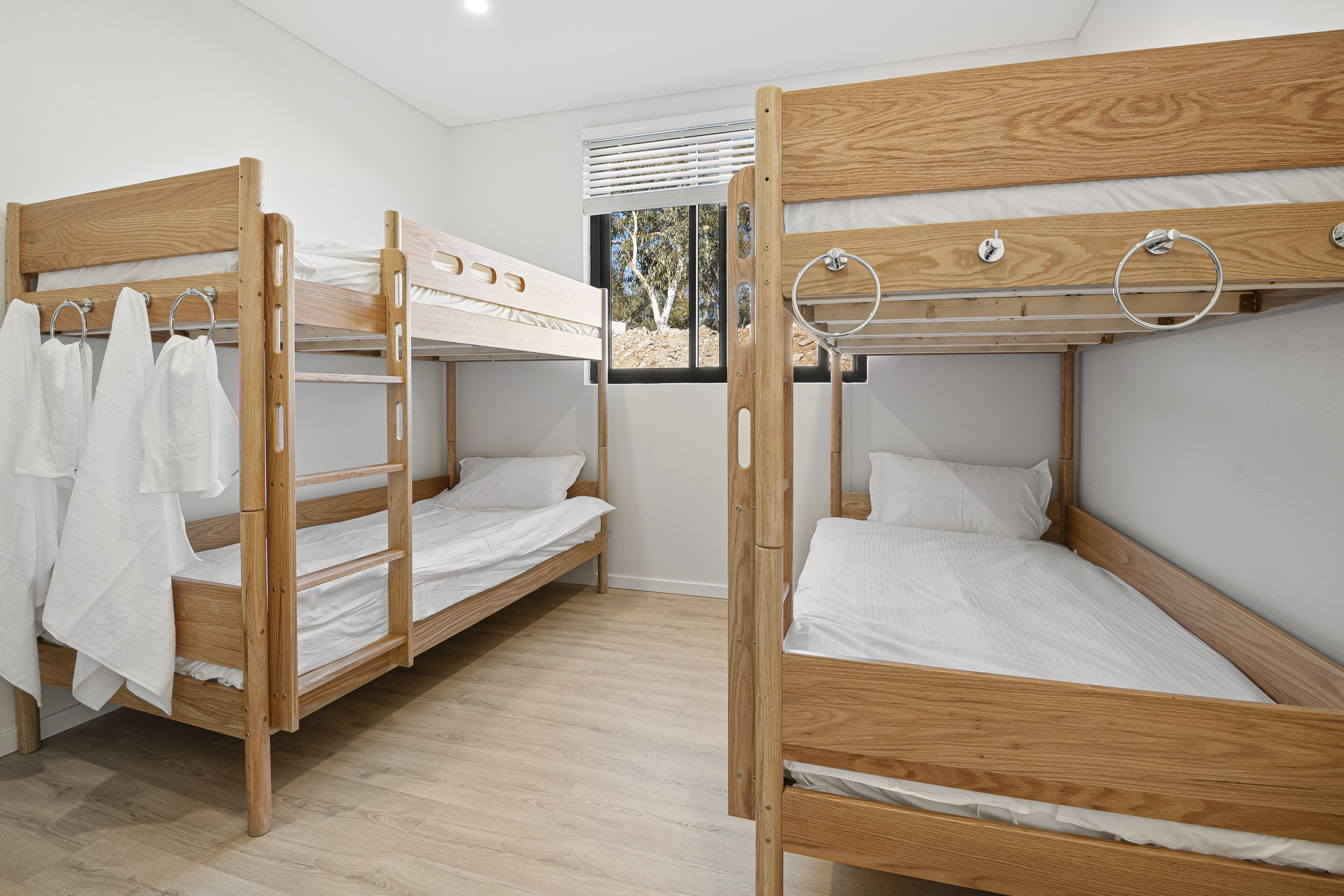 Quarto com três beliches, cada um com estrutura de madeira e roupa de cama branca.