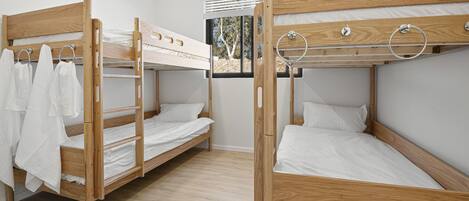 Quarto com três beliches, cada um com estrutura de madeira e roupa de cama branca.