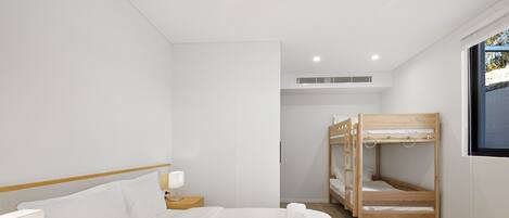 Moderni hotellihuone, jossa on suuri sänky, puinen kerrossänky, yöpöytä lampulla ja ikkuna, josta on näkymä.