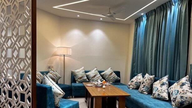 A modern living room with a blue sofa set, a wooden coffee table, and a patterned floor lamp. - Hotel Grand Riviera (Paonta Sahib)