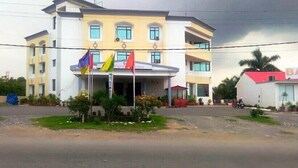 A multi-story hotel with a central entrance, multiple flags, and a parking area in front. - Hotel Grand Riviera (Paonta Sahib)