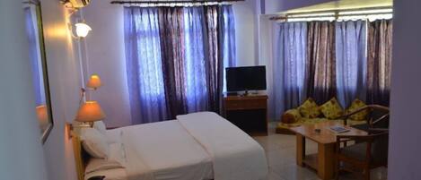A hotel room with a bed, a TV, a desk with a chair, and curtains.